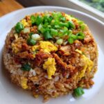 A mound of freshly made chicken fried rice topped with scrambled egg and bright green scallions.