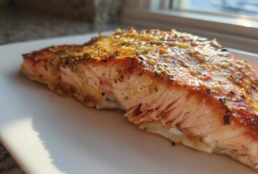 Close-up of a flaky, seasoned piece of air fryer salmon resting on a white plate.