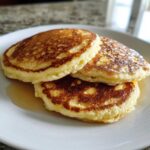 A stack of three fluffy almond flour pancakes drizzled with syrup on a white plate.