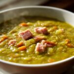 Close-up of a thick, green pea soup topped with diced ham and carrots, perfect for comfort.