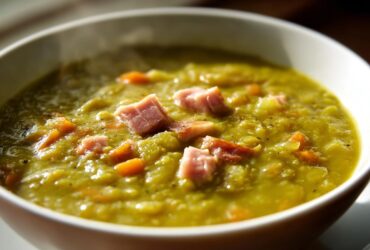 Close-up of a thick, green pea soup topped with diced ham and carrots, perfect for comfort.
