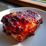 Close-up of a juicy piece of bbq chicken coated in a thick, glossy, caramelized sauce.