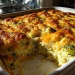 Close-up of a baked broccoli casserole in a white dish, featuring a bubbly, golden-brown cheese crust.