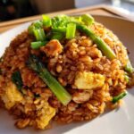 A mound of savory chicken fried rice featuring scrambled egg, asparagus spears, and topped with fresh green onions.