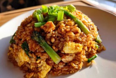 A mound of savory chicken fried rice featuring scrambled egg, asparagus spears, and topped with fresh green onions.