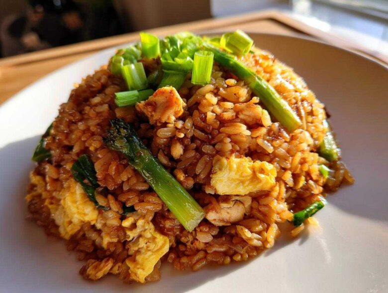 A mound of savory chicken fried rice featuring scrambled egg, asparagus spears, and topped with fresh green onions.