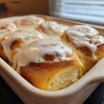 Close-up of warm, glazed cinnamon roll pastries baked together in a white dish.