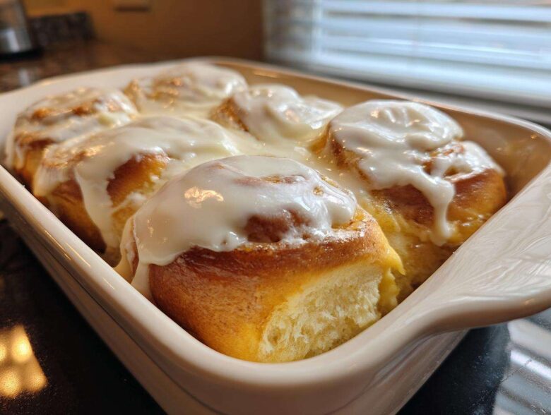 Close-up of warm, glazed cinnamon roll pastries baked together in a white dish.