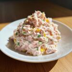 A mound of creamy, shredded ham salad mixed with yellow and green ingredients, served on a white plate.