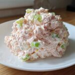A mound of creamy pink ham salad mixed with visible chunks of green celery served on a white plate.