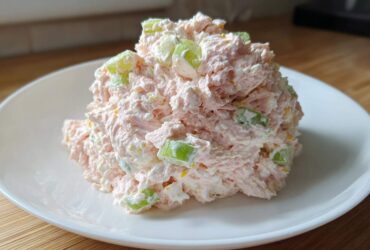 A mound of creamy pink ham salad mixed with visible chunks of green celery served on a white plate.
