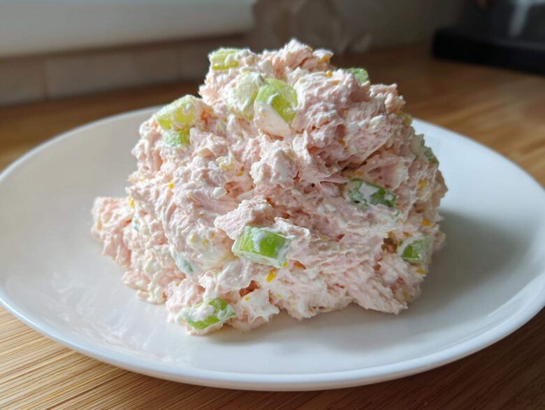 A mound of creamy pink ham salad mixed with visible chunks of green celery served on a white plate.