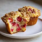 Close-up of a strawberry muffin cut in half showing moist cake and fresh strawberries, topped with a streusel crumb topping. These are amazing strawberry muffins.