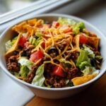 A close-up view of a delicious taco salad featuring seasoned ground beef, lettuce, tomatoes, black olives, shredded cheese, and tortilla chips.