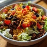 A vibrant close-up of an amazing taco salad featuring seasoned ground beef, shredded cheese, tomatoes, olives, and tortilla chips over lettuce.