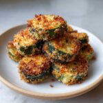 A stack of golden brown, crispy baked parmesan zucchini slices piled high on a light-colored plate.