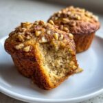 Close-up of a moist banana nut muffin with a bite taken out, showing the crumb texture and walnut topping.