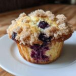 A close-up of a golden blueberry muffin topped with a generous layer of sugary streusel crumb topping.