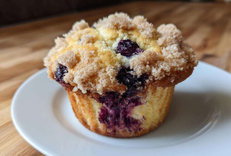 A close-up of a golden blueberry muffin topped with a generous layer of sugary streusel crumb topping.