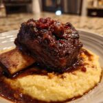 A single serving of rich, dark braised short ribs resting on a bed of creamy yellow polenta.