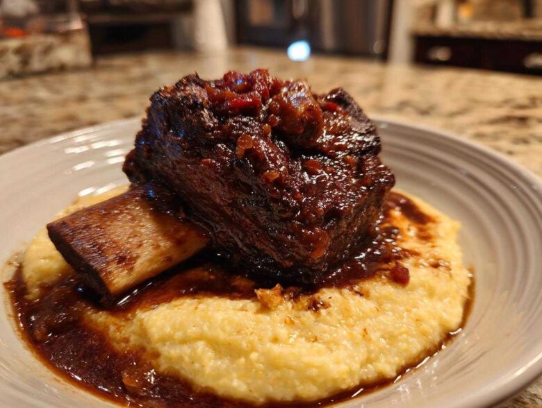 A single serving of rich, dark braised short ribs resting on a bed of creamy yellow polenta.