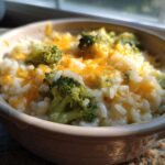 Close-up of cheesy broccoli rice topped with melted cheddar cheese in a small ceramic bowl.