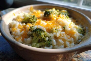 Close-up of cheesy broccoli rice topped with melted cheddar cheese in a small ceramic bowl.