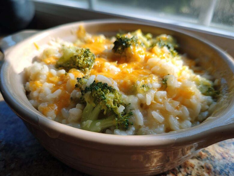 Close-up of cheesy broccoli rice topped with melted cheddar cheese in a small ceramic bowl.