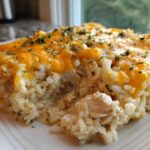 A close-up serving of cheesy chicken and rice casserole topped with melted cheddar and parsley.
