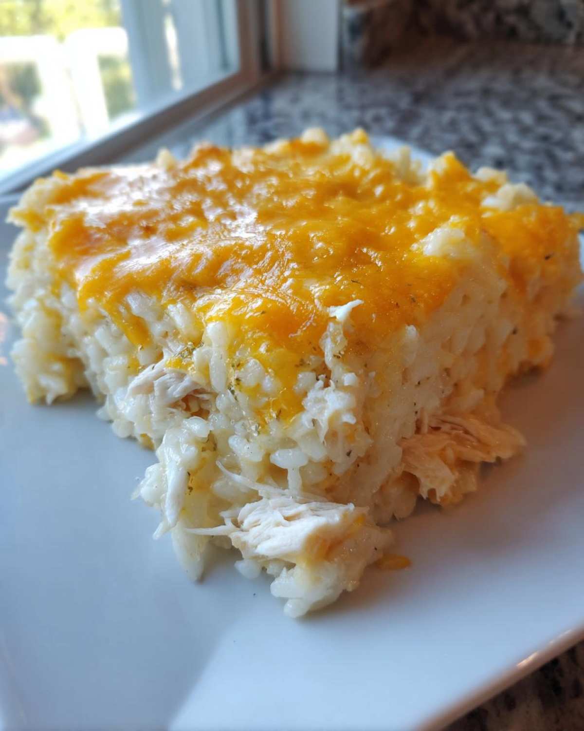 A close-up serving of cheesy chicken and rice casserole topped with melted cheddar cheese.