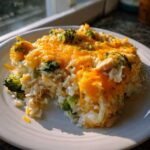 A hearty serving of chicken broccoli rice casserole topped with melted cheddar cheese on a white plate.