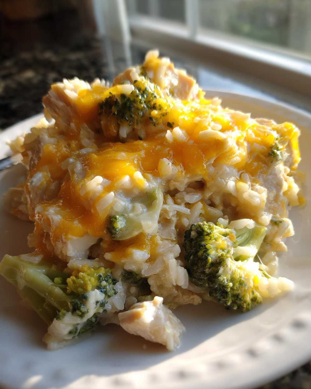 Close-up of a serving of creamy chicken broccoli rice casserole topped with melted cheddar cheese.