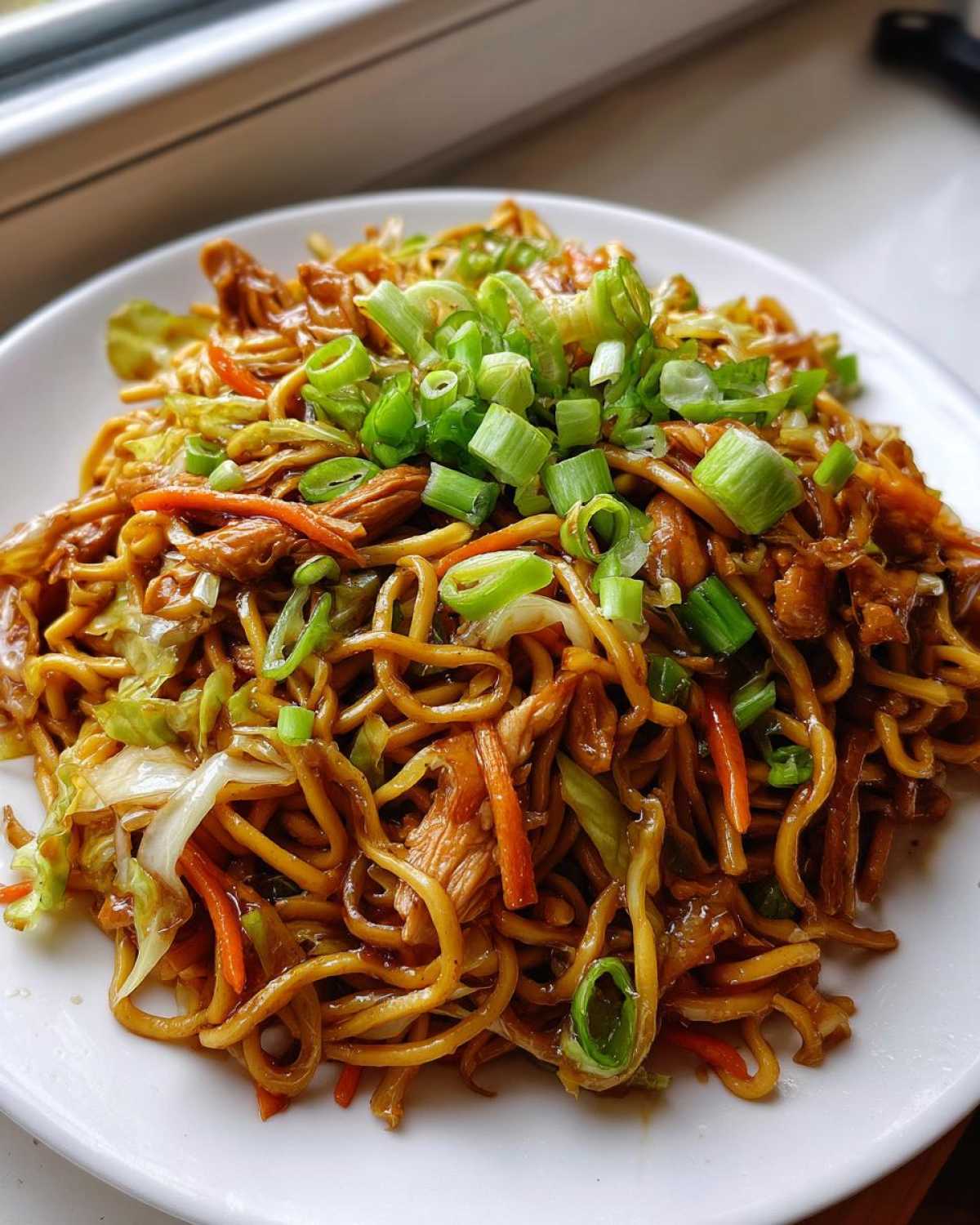 Close-up of a plate featuring a serving of savory chicken chow mein recipe, topped with fresh green onions.