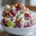 A close-up of creamy chicken salad chick grape salad featuring red and green grapes, topped with a brown sugar glaze.