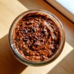 Overhead view of rich chocolate overnight oats topped with dark chocolate shavings in a glass jar.