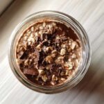 Overhead view of creamy chocolate overnight oats topped with dark chocolate chunks in a glass jar.