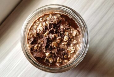 Overhead view of creamy chocolate overnight oats topped with dark chocolate chunks in a glass jar.