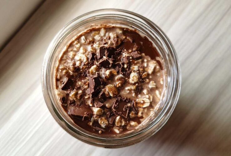 Overhead view of creamy chocolate overnight oats topped with dark chocolate chunks in a glass jar.