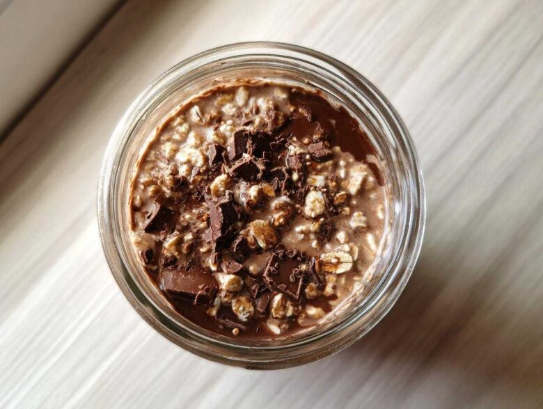 Overhead view of creamy chocolate overnight oats topped with dark chocolate chunks in a glass jar.