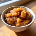 A close-up of chunky, homemade applesauce seasoned with cinnamon served in a white bowl.