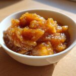 Close-up of chunky, spiced applesauce served in a small white bowl, highlighted by sunlight.