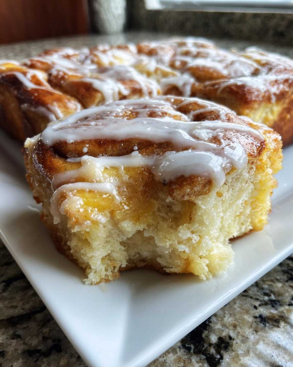 A close-up of a soft, fluffy piece of Cinnamon roll casserole with a bite taken out, drizzled with white icing.