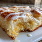 A close-up, appetizing shot of a square serving of moist cinnamon roll casserole topped with thick white icing.