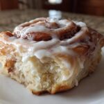 Close-up of a soft cinnamon roll generously topped with thick, white cream cheese frosting.