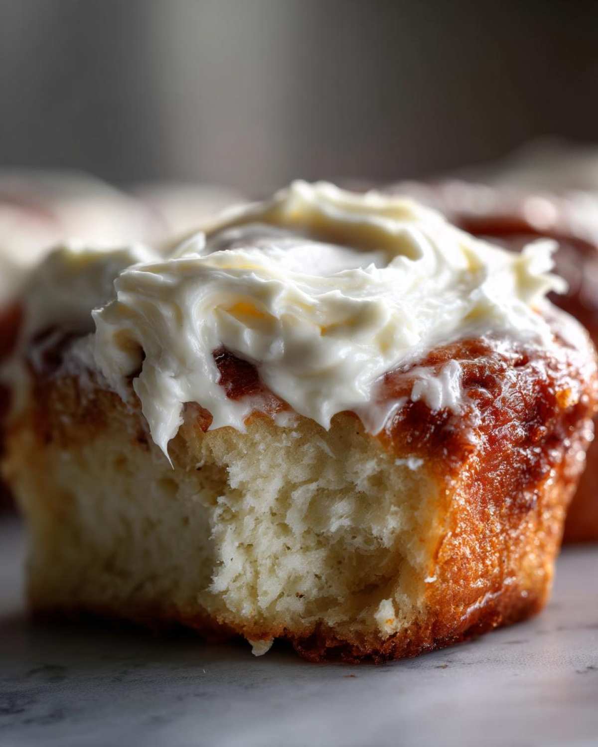 Close-up of a fluffy cinnamon roll topped generously with thick, white cream cheese frosting.