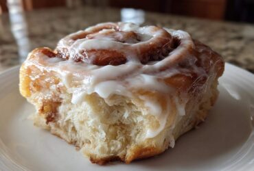 Close-up of a soft cinnamon roll generously topped with thick, white cream cheese frosting.