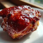 Close-up of a piece of succulent bbq chicken coated in thick, glossy, dark red barbecue sauce.