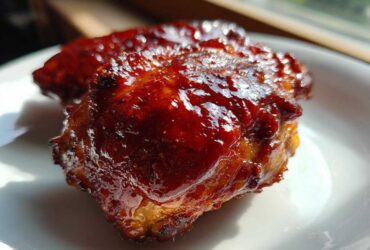 Close-up of a piece of succulent bbq chicken coated in thick, glossy, dark red barbecue sauce.