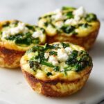 Close-up of three golden Cottage Cheese Egg Cups With Spinach & Feta topped with crumbled white cheese.