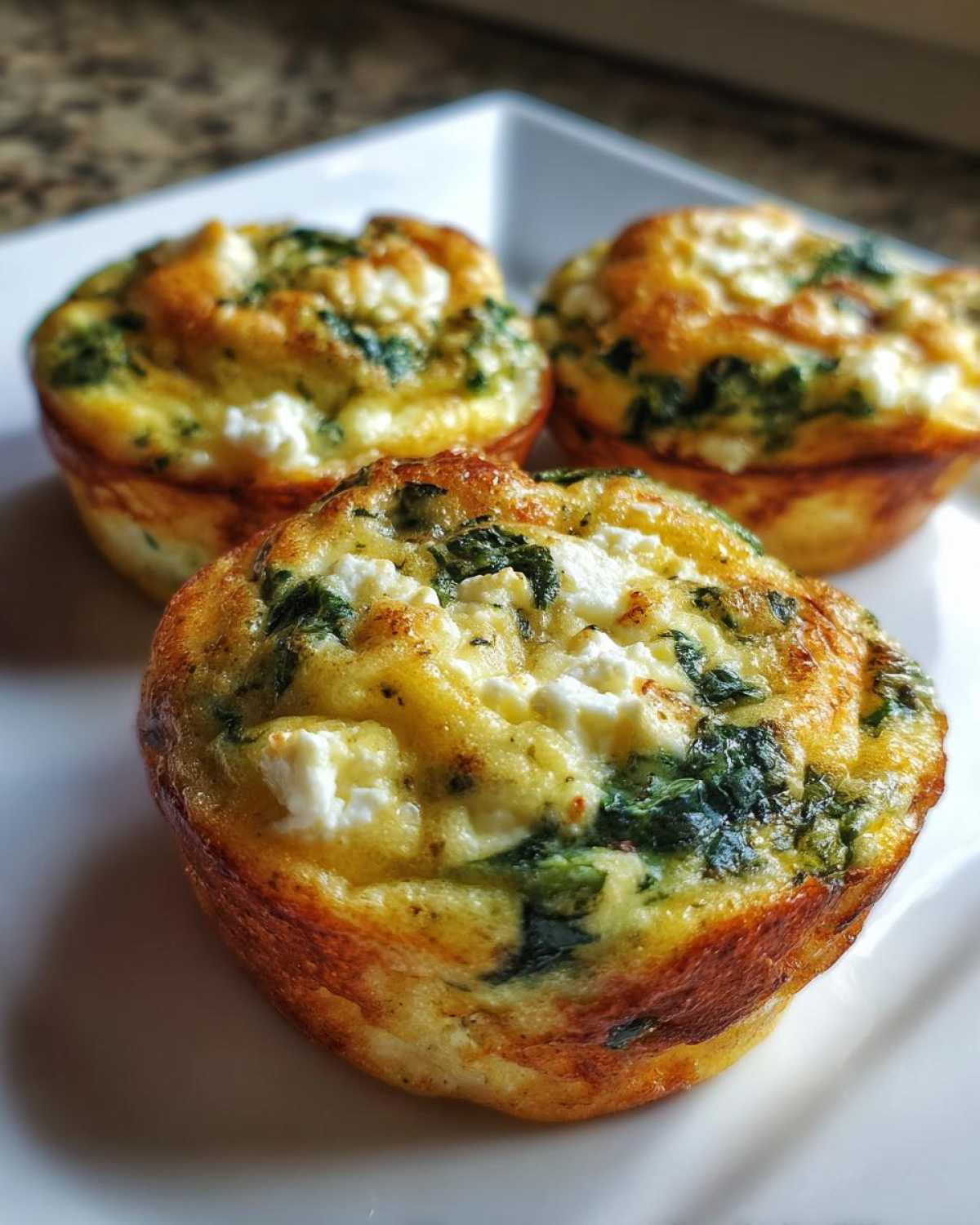 Close-up of three golden brown Cottage Cheese Egg Cups With Spinach & Feta served on a white plate.